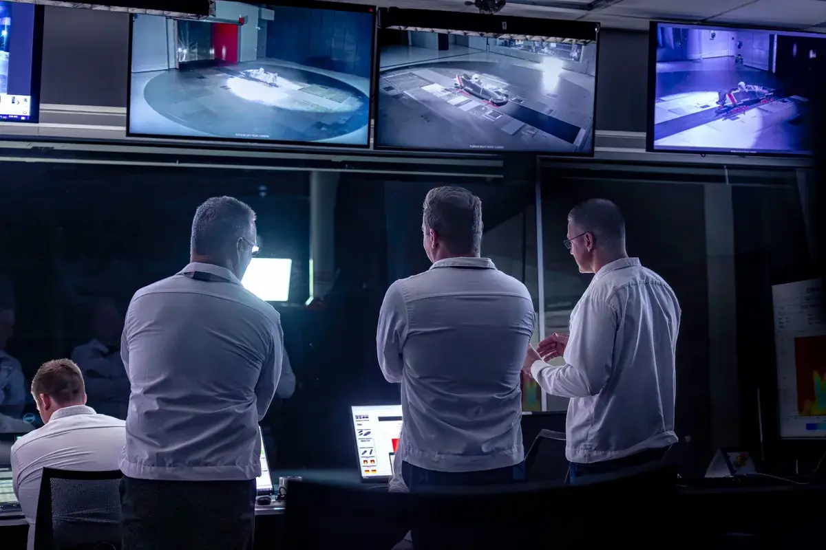 three men watch monitors