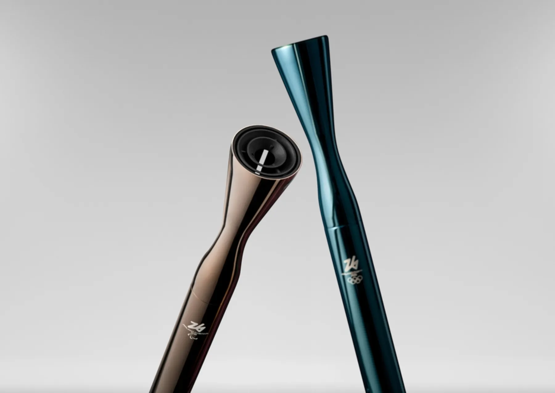 the gold 2026 winter paralympic torch next to the blue winter olympic torch