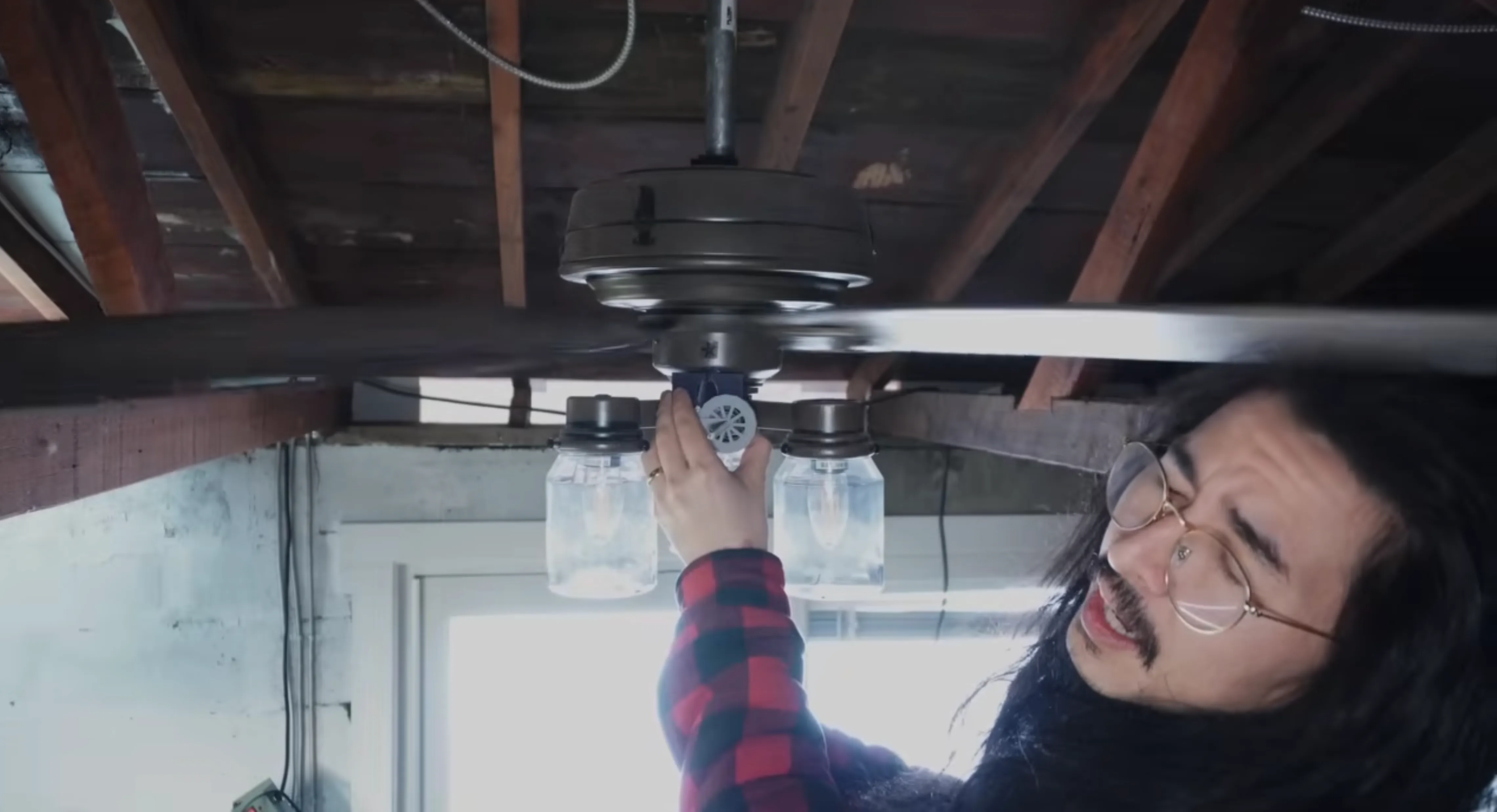 a man ducks down underneath a ceiling fan 
