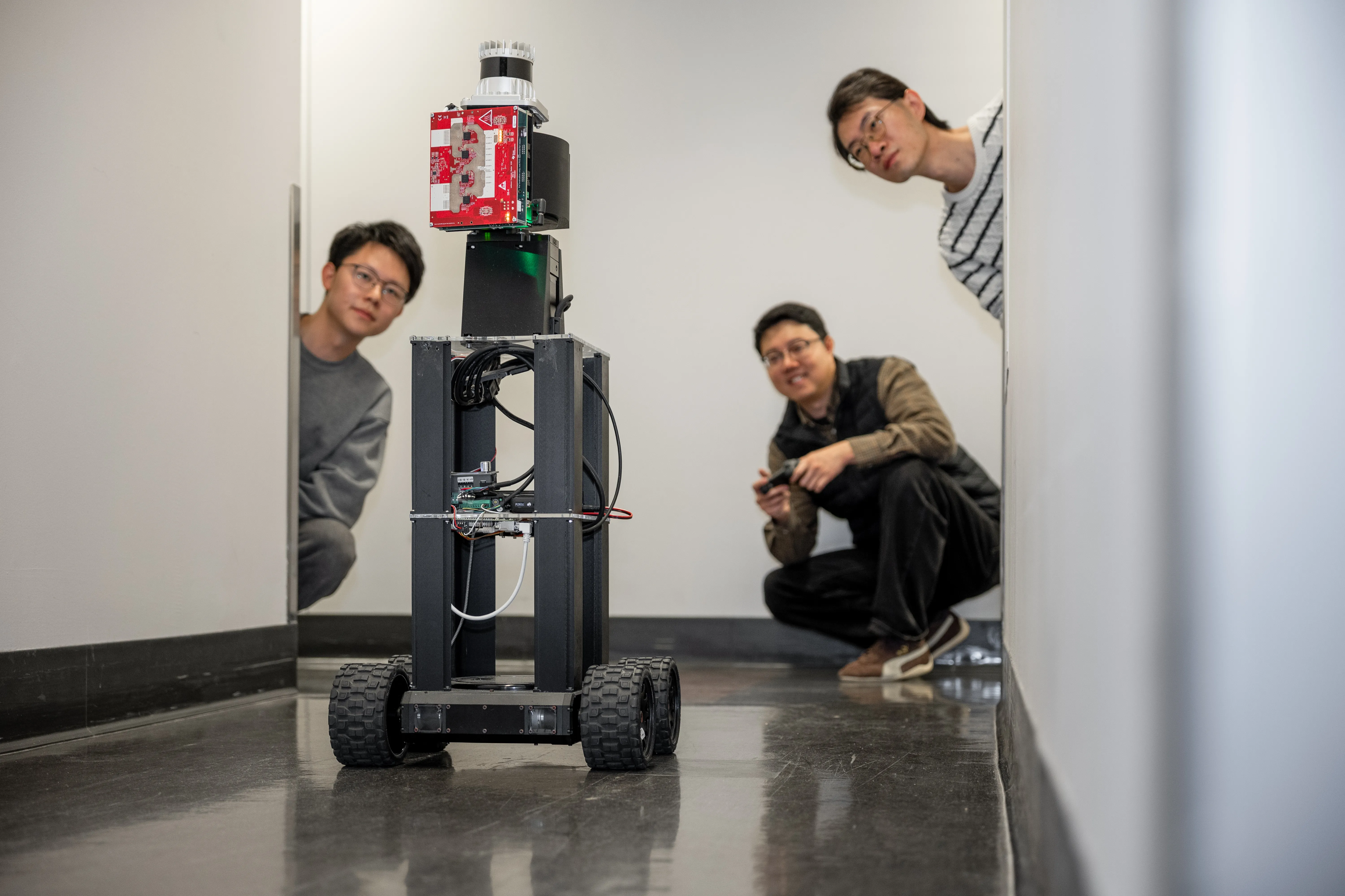 three men test a tall robot on four wheels in a hallway