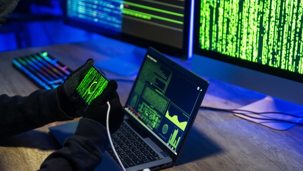 A scene of a hacker engaging in cybersecurity breaches using advanced technology and devices in a dimly lit environment.