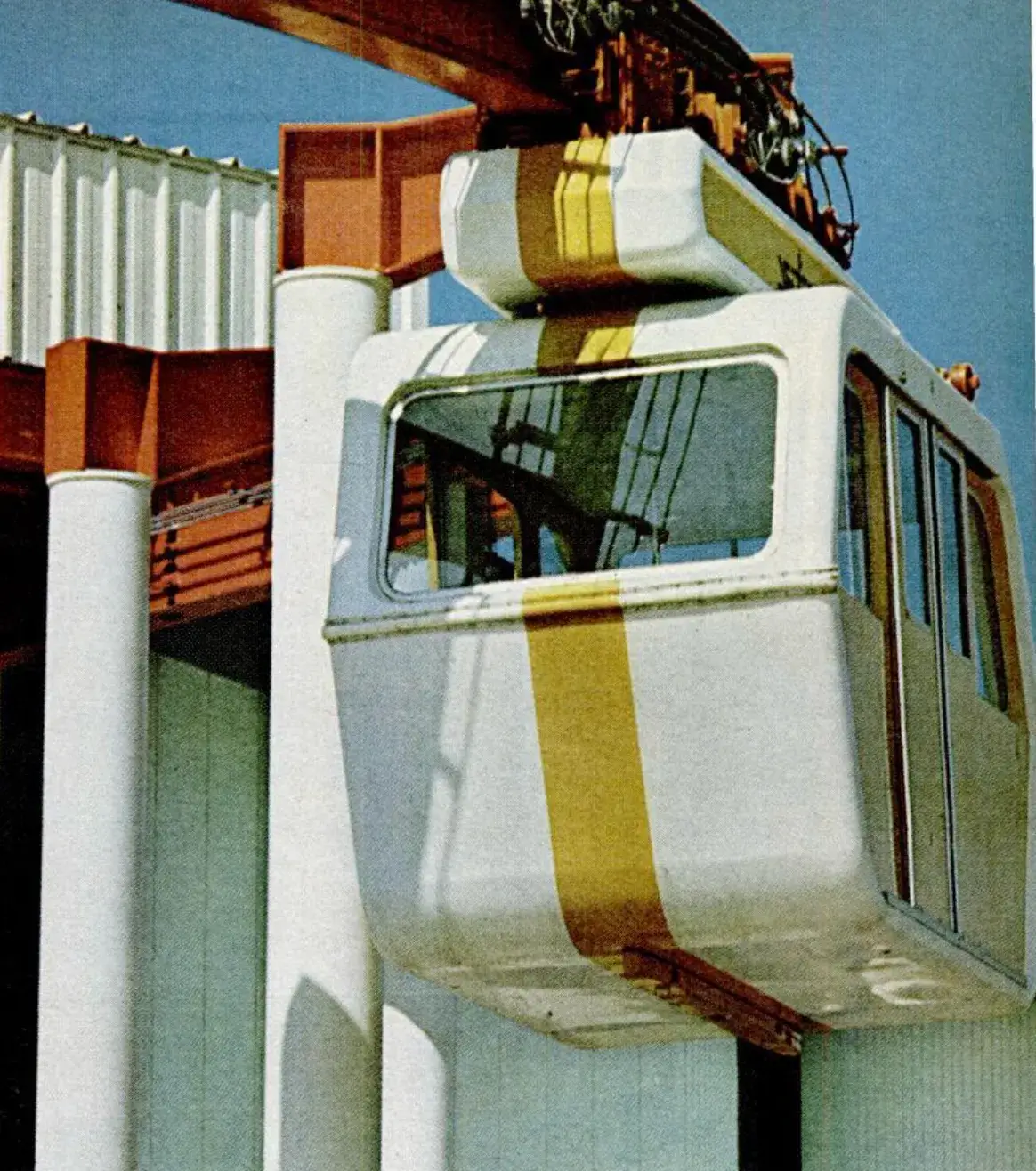 Vintage photograph showing a suspended car that hangs from a track on the roof. The car is white with a yellow stripe.