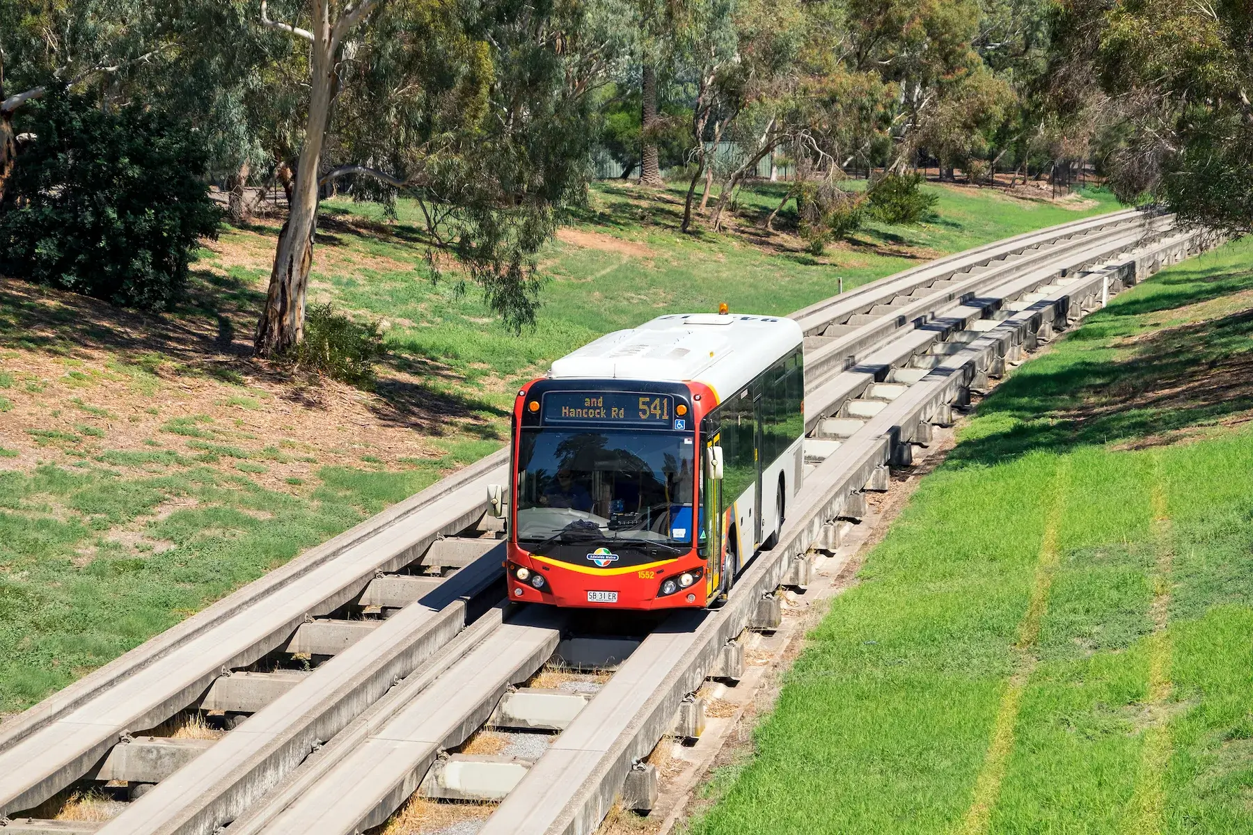 Adelaide, Australia - March 21, 2016: New series of Adelaide Metro bus on Route 541 heads away from the city centre along the O-Bahn guided Busway with a backdrop of trees and open space. Opened in 1986 after a light rail (tram) extension was rejected, the Daimler-Benz O-Bahn system runs on specially-built concrete track incorporating elements of both bus and rail systems. Adelaide’s unique busway is 12km (7.5mi) long and incorporates 3 interchange stations.