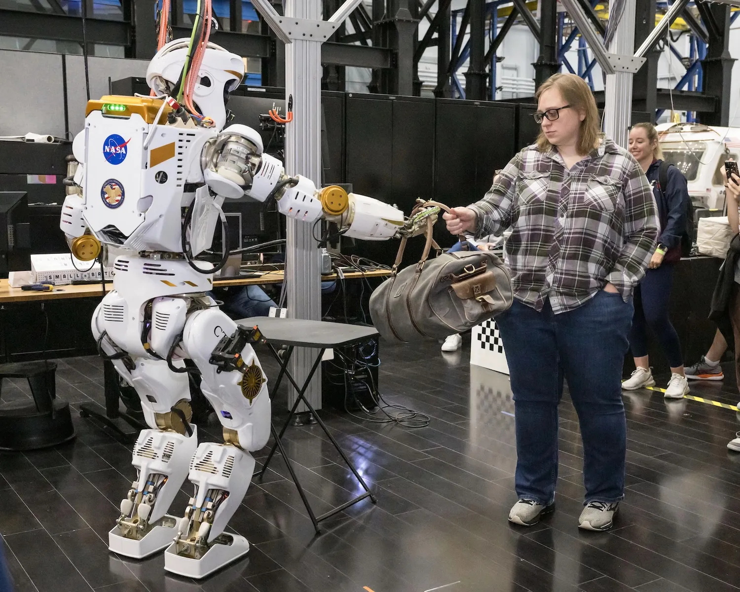 Робот Valkyrie передаёт сотруднице Dexterous Robotics Team Эмме Землер спортивную сумку во время демонстрации в 2024 году