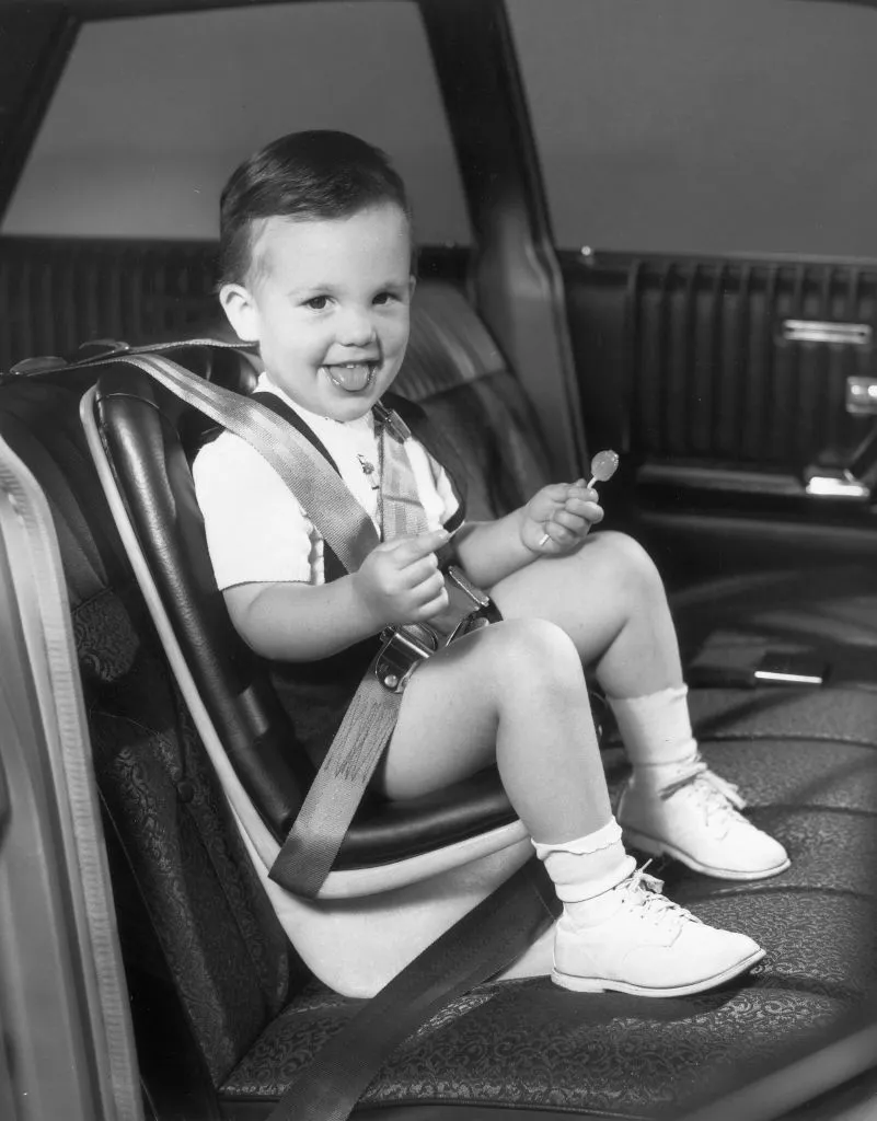 Мальчик с леденцом сидит в Jeenay Car Seat в автомобиле, 1960-е годы.